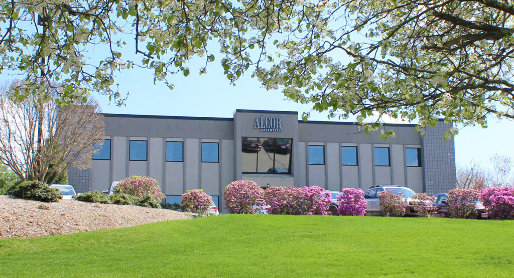 Front view of the ALCOR Scientific building with flowers and parked cars.
