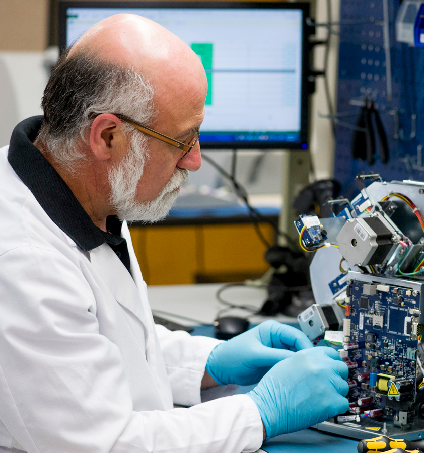 Picture of a male engineer wearing glasses in a white lab gown and blue gloves trying to repair an ESR device.